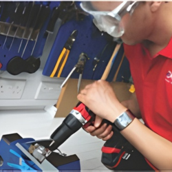 Person using a power drill on a metal part in a workshop.