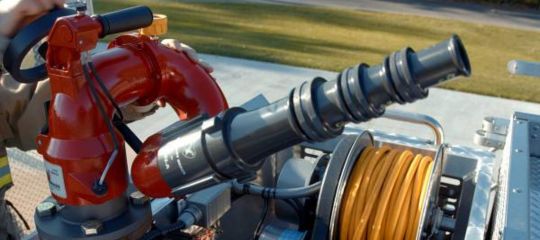 Red fire monitor and nozzle assembly with hose reel on top of a fire apparatus.