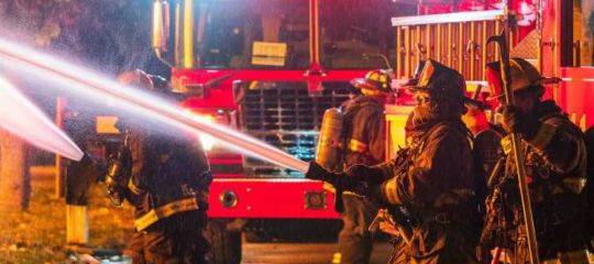 Firefighters using water hoses in front of a fire truck at night.